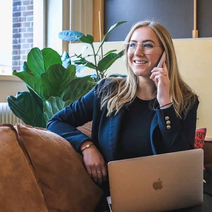 Medewerker van het administratiekantoor belt met een klant, met haar laptop op schoot