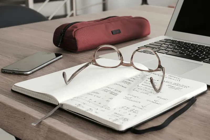 Opengeslagen notitieboek met bril naast een laptop op een houten bureau
