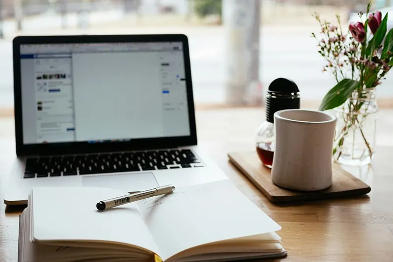 Laptop en opengeslagen notitieboek op een tafel bij het raam